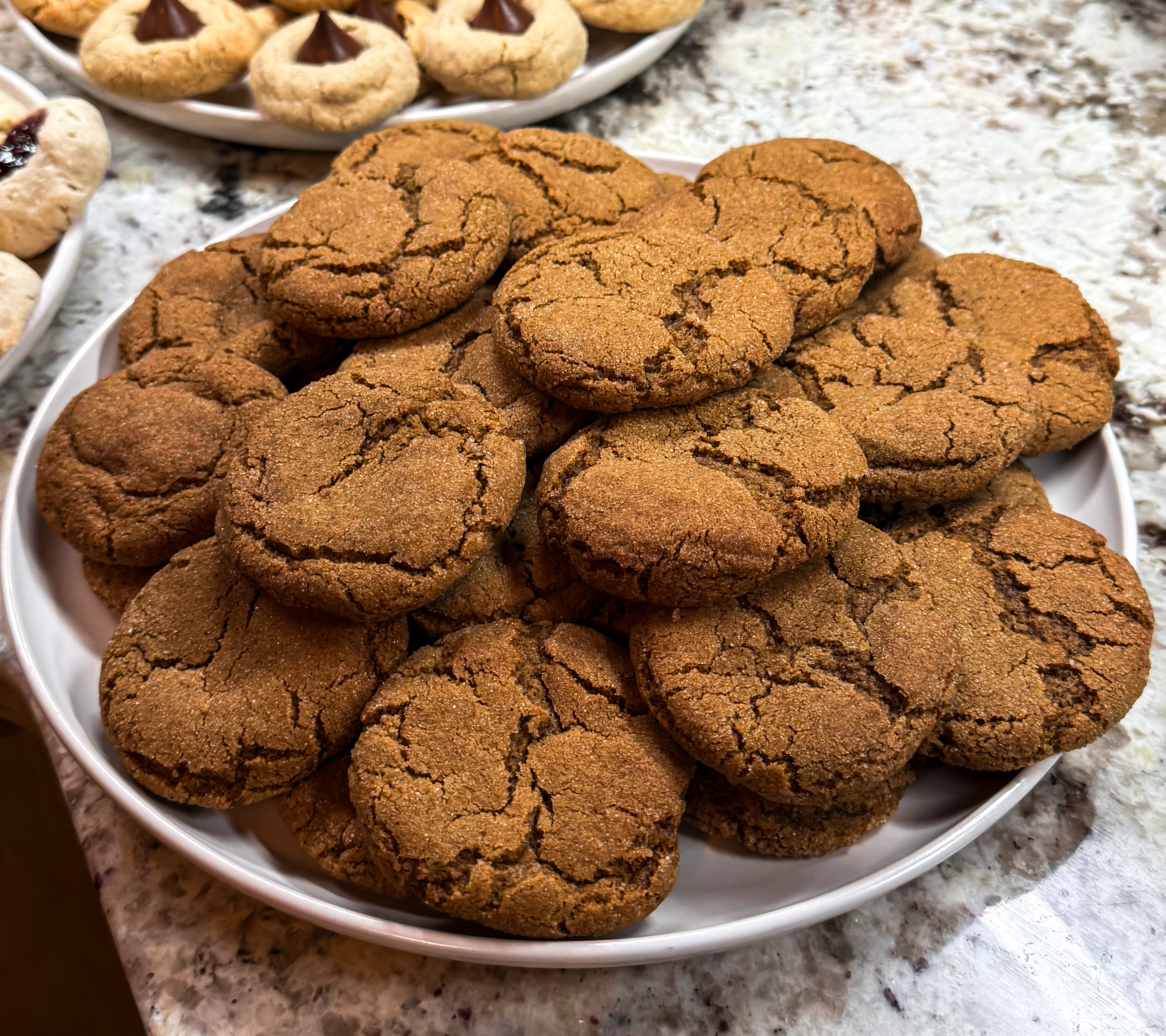 A close-up of a plate filled with golden brown, soft molasses cookies with cracked tops.