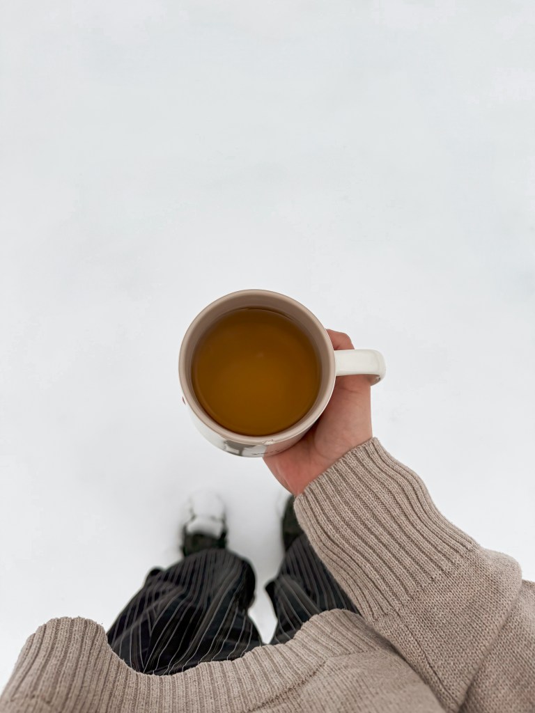 Hand holding a white mug filled with herbal tea against a snowy winter backdrop.